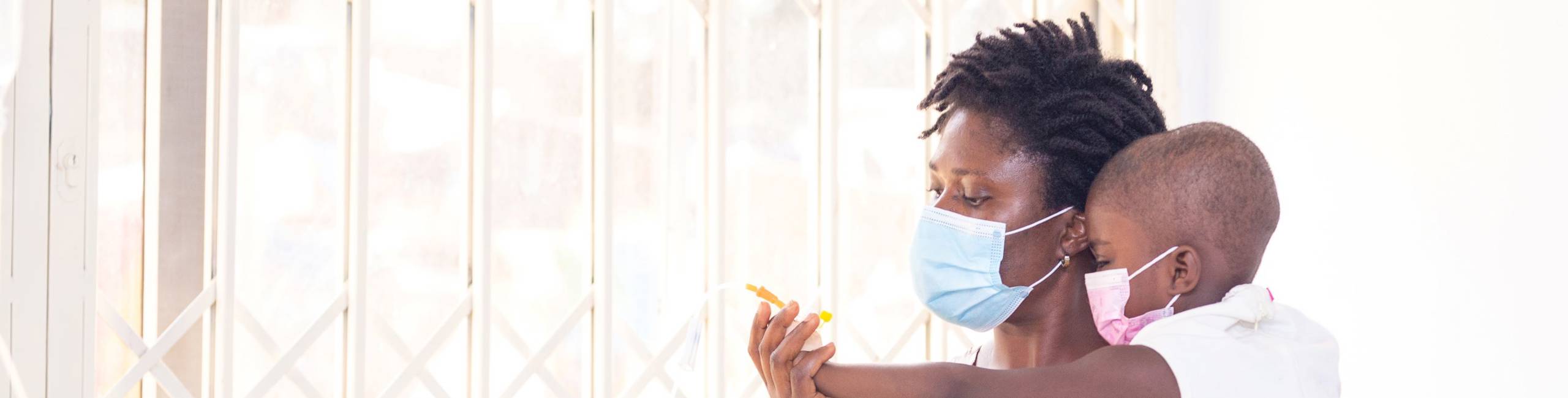 A woman holding a child, both wearing protective face masks